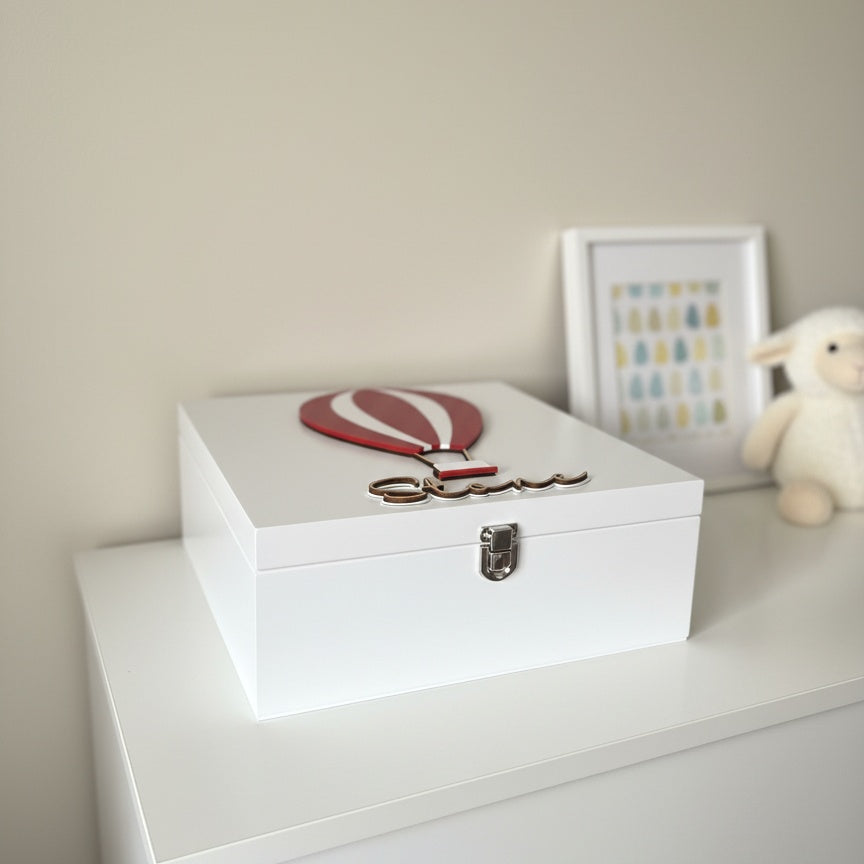 White baby keepsake box with a red and white balloon on top of a white dresser.