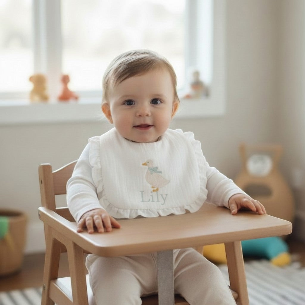 The Wee Rhubarb Gift Co Ltd white muslin baby bib with embroidered duck, mint bow, ruffles, and name 'Lily'.