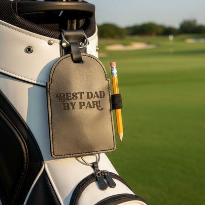 Golf bag with 'Best Dad By Par' tag and pencil on a golf course
