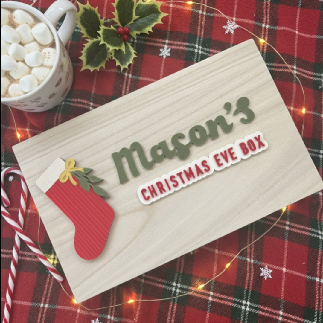 Christmas eve wooden box with 'Mason's Christmas Eve Box' on a plaid background with a mug of hot chocolate.
