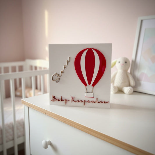 Baby keepsake box with red hot air balloon design on a dresser in a nursery.