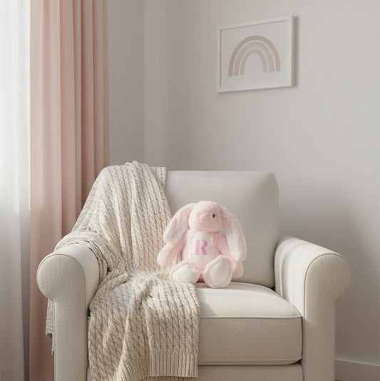 Beige armchair with a pink bunny toy and knitted blanket in a room with pink curtains and a rainbow painting.