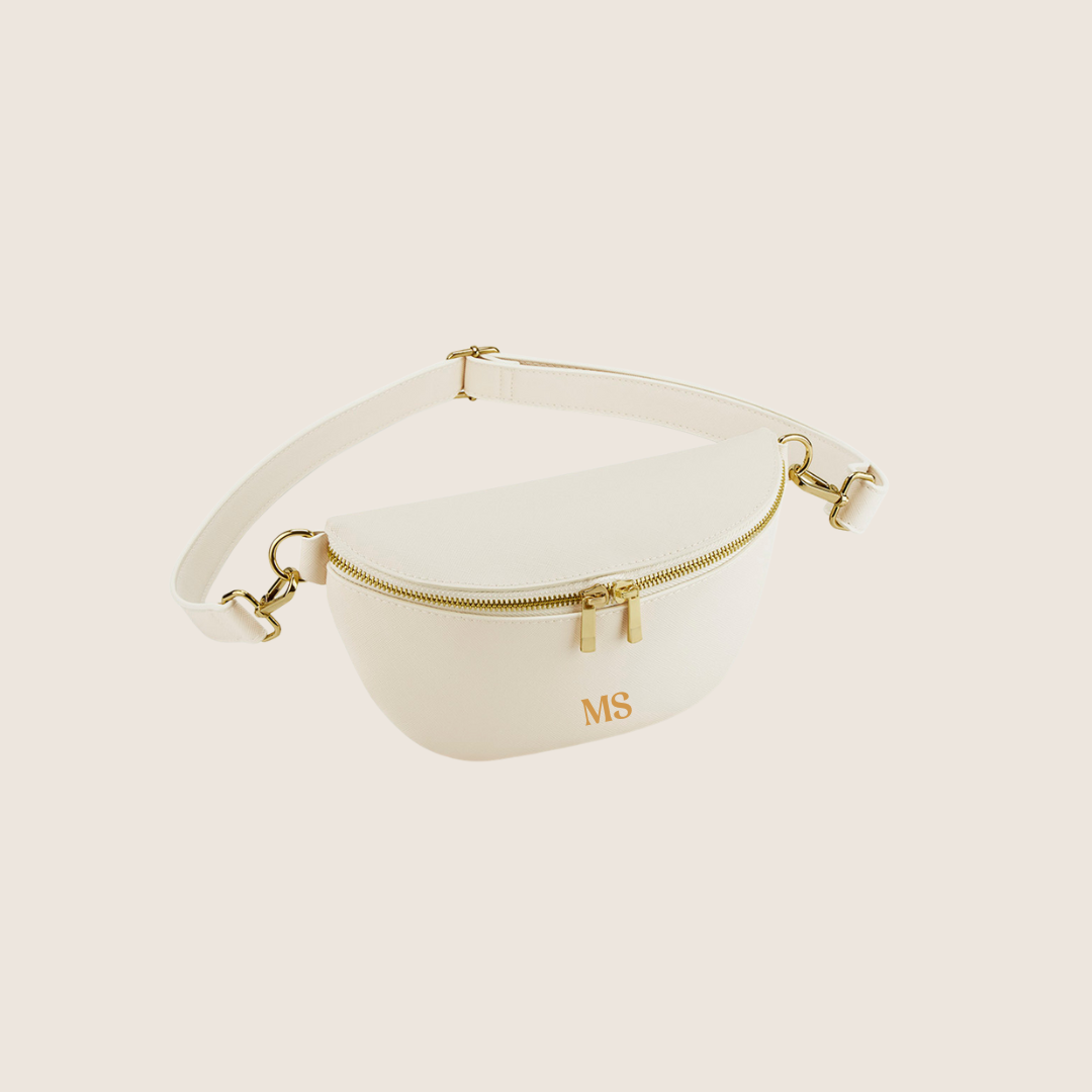 White waist/belt bag with gold accents and initials on a light beige background