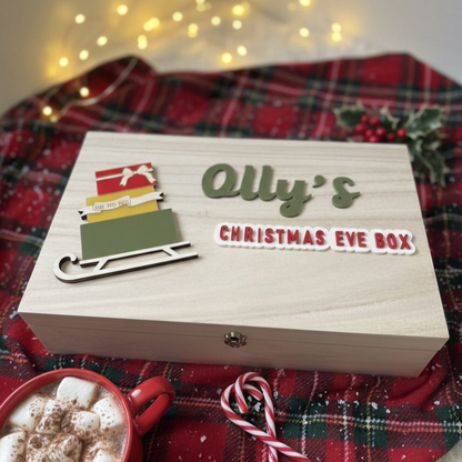 Wooden Christmas Eve box with personalized name, surrounded by festive decor and a mug of hot chocolate.