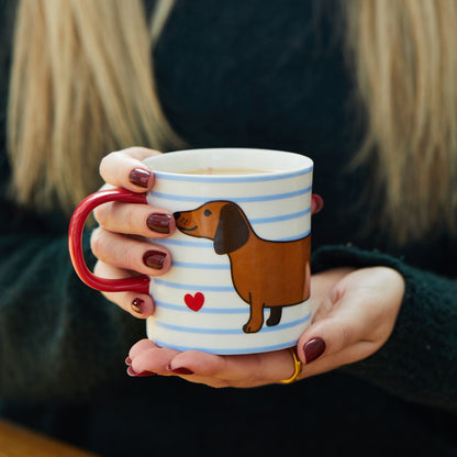 Person holding a mug with a dachshund design and red heart.