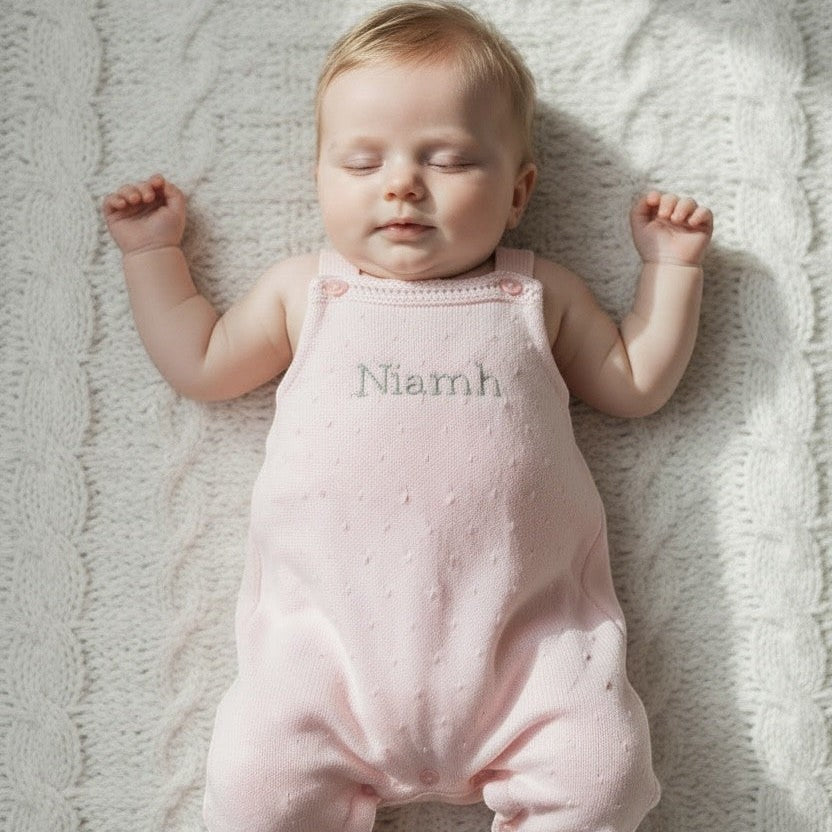 Baby in a pink romper with 'Niamh' embroidered on it, lying on a textured blanket.