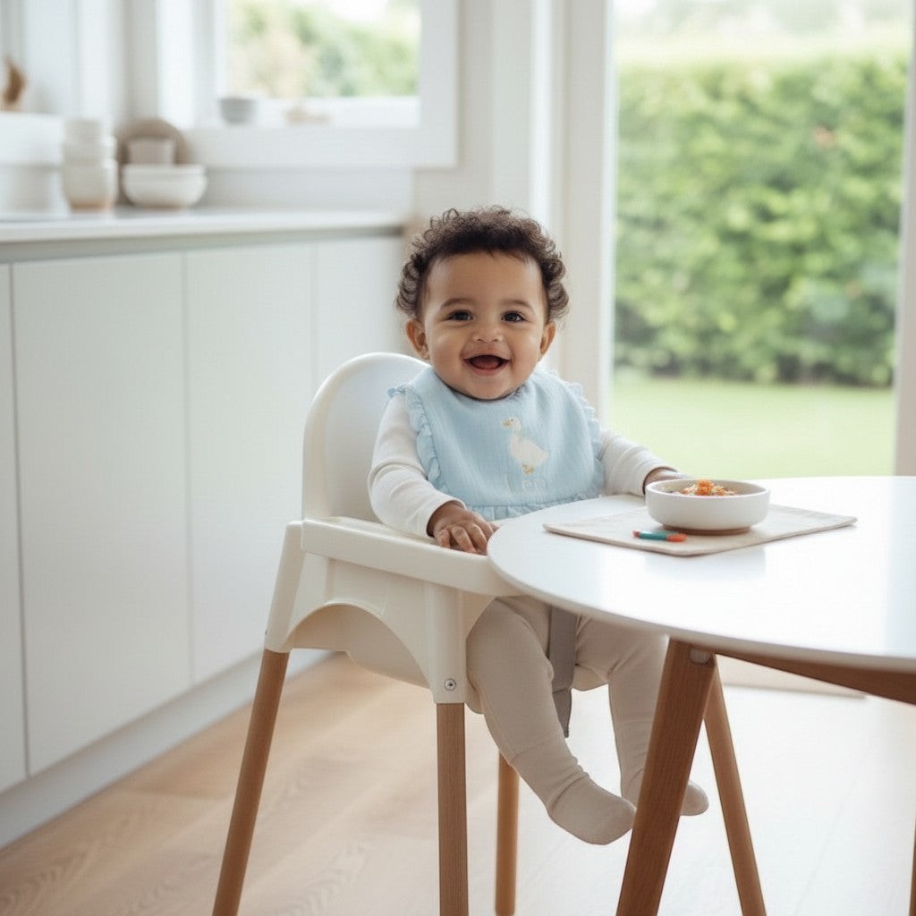 The Wee Rhubarb Gift Co Ltd light blue muslin baby bib with embroidered goose and ruffle trim. Baby girl sitting in high chair.