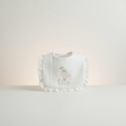The Wee Rhubarb Gift Co Ltd white muslin baby bib with embroidered duck, blue bow, ruffles and name 'Lily'.
