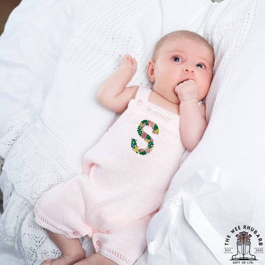 The Wee Rhubarb Gift Co Ltd pastel pink knitted baby romper with embroidered floral letter S. Soft knit fabric, button fastenings.