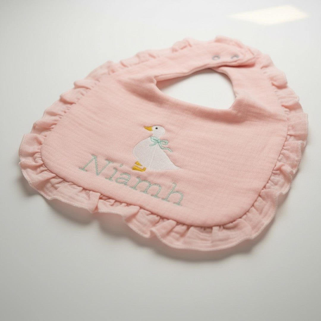 The Wee Rhubarb Gift Co Ltd light pink muslin baby bib with embroidered goose and name 'Niamh', ruffled edge.