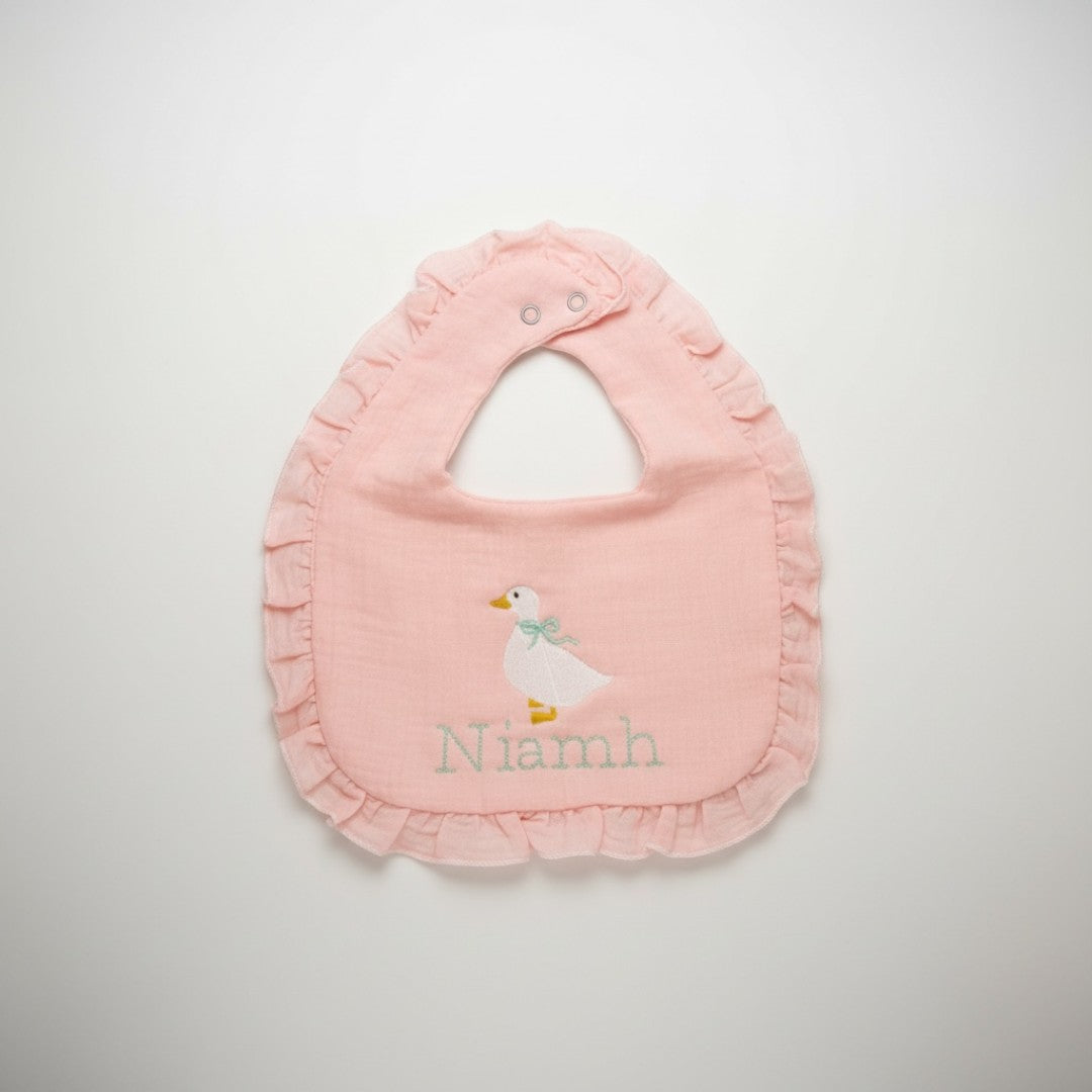 The Wee Rhubarb Gift Co Ltd light pink muslin baby bib with embroidered goose and mint green bow, ruffle trim, and name personalization.
