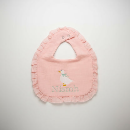 The Wee Rhubarb Gift Co Ltd light pink muslin baby bib with embroidered goose and mint green bow, ruffle trim, and name personalization.