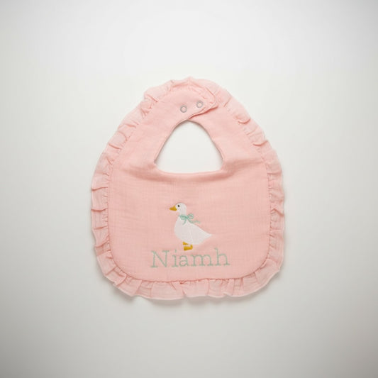 The Wee Rhubarb Gift Co Ltd light pink muslin baby bib with embroidered goose and mint green bow, ruffle trim, and name personalization.